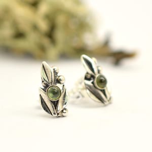 May include: A pair of silver earrings with a green gemstone set in a leaf design.