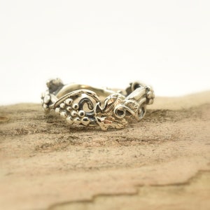 Op de afbeelding: Een zilveren ring met een wijnstokontwerp. De ring toont gedetailleerde afbeeldingen van druiven, bladeren en wijnstokken.