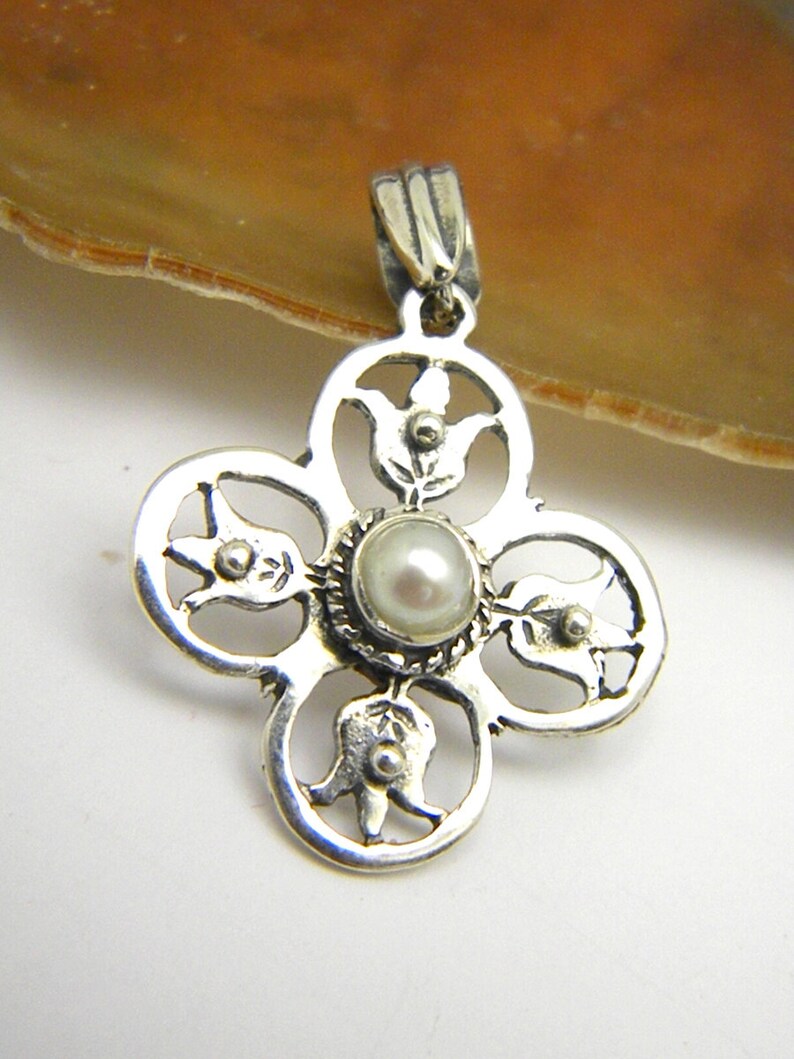 May include: Silver pendant featuring a delicate floral design with a white pearl at its centre.