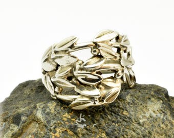 Può includere: Un anello d'argento con un designo di foglie e rami. L'anello è su una roccia grigia.
