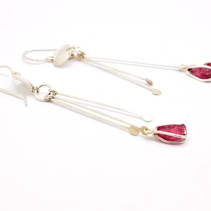 Könnte beinhalten: Ein Paar silberne Ohrringe mit rosa Edelstein-Tropfen. Die Ohrringe haben mehrere silberne Stränge, die von oben hängen.