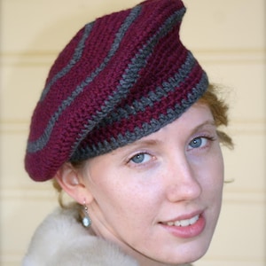 May include: A woman wearing a burgundy and gray striped crocheted beret. She is wearing a white fur coat.