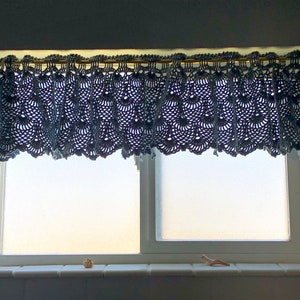 May include: A window with a blue crocheted valance and a white window frame. The window is closed and the glass is frosted.