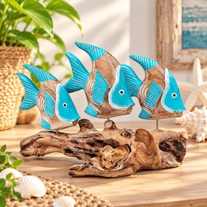 Puede incluir: Una escultura decorativa que presenta tres figuras de peces talladas en madera con detalles pintados en turquesa brillante en las aletas y cabezas. Los peces están montados sobre una pieza de madera flotante natural, creando un conjunto acuático.