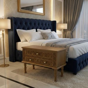 Puede incluir: Un dormitorio con cabecero y estructura de cama azul marino con mechones. Una mesita de noche de madera marrón claro con diseños florales tallados se encuentra al pie de la cama. Ropa de cama blanca y una manta estampada.