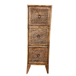 Könnte beinhalten: Ein hoher Holzschrank mit drei Schubladen und aufwendigen Blumenschnitzereien auf jeder Schublade. Der Schrank hat eine warme braune Farbe und kleine, runde Metallgriffe. Er steht auf vier kurzen Beinen.