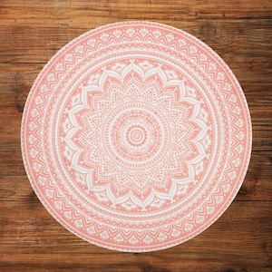 Puede incluir: Un dise&ntilde;o de mandala redondo rosa y blanco. El intrincado patr&oacute;n presenta un motivo floral central rodeado de c&iacute;rculos conc&eacute;ntricos de patrones sim&eacute;tricos detallados. El dise&ntilde;o est&aacute; sobre un fondo de madera, creando un contraste de texturas.