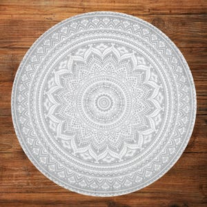 May include: A round, gray and white mandala-patterned rug. The intricate design features a central floral motif surrounded by detailed, symmetrical patterns. The rug is placed on a wooden surface.