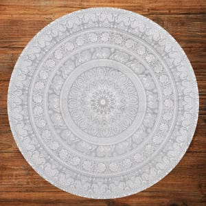 Puede incluir: Un tapiz mandala redondo, gris claro, con intrincados patrones blancos. El dise&ntilde;o presenta motivos florales y de elefantes dispuestos en c&iacute;rculos conc&eacute;ntricos, creando una est&eacute;tica detallada y sim&eacute;trica. El tapiz est&aacute; colocado sobre una superficie de madera.
