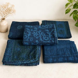 May include: Four folded rectangular fabric quilts in shades of deep indigo and navy blue. Each quilt features intricate tonal stitching and varied patterns, including floral motifs, geometric borders, and leaf designs, all with visible hand-stitched details.
