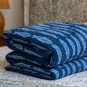 Könnte beinhalten: Gefaltete indigoblaue Steppdecke mit einem sich wiederholenden Fischmuster. Die Steppdecke ist aus weichem Stoff gefertigt und hat weiße Nähte. Die Steppdecke ist auf einer anderen Steppdecke mit einem ähnlichen Muster gestapelt.
