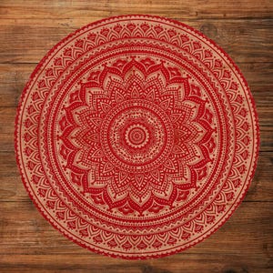 May include: A round red and beige mandala design. The intricate pattern features a central floral motif surrounded by detailed symmetrical elements. The design is set against a wooden background, creating a contrast of textures and colors.