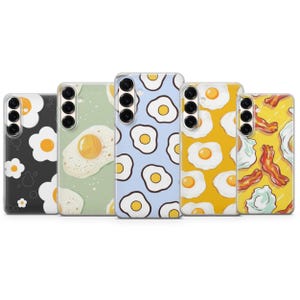 Könnte beinhalten: Eine Sammlung von Handyhüllen mit Frühstücksmotiven. Die Hüllen zeigen Muster von Spiegeleiern, Speck und floralen Motiven in verschiedenen Farben, darunter Schwarz, Grün, Blau und Gelb. Jede Hülle hat einen Kameraausschnitt und Tastenanordnungen.