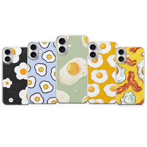Könnte beinhalten: Fünf Handyhüllen mit Frühstücksmotiven. Die Hüllen zeigen Muster von Spiegeleiern, Speck und floralen Designs. Die Farbpalette umfasst Schwarz, Blau, Gelb und Grün. Jede Hülle hat einen Kameraausschnitt.