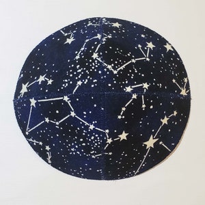 May include: A dark blue kippah with a white constellation pattern. The kippah is made of a soft, textured fabric.