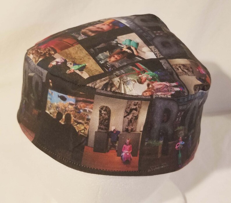 Op de afbeelding: Een zwarte stoffen kippa met een collage van foto's erop gedrukt. De foto's zijn van verschillende mensen en plaatsen, waaronder een gezin, een museum en een strand.