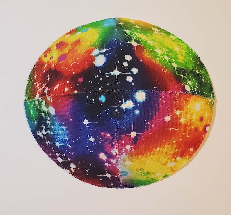 Pu&ograve; includere: Una kippah rotonda e colorata con una stampa a galassia. La kippah &egrave; realizzata in tessuto e ha uno sfondo blu scuro con stelle bianche e nebulose colorate.