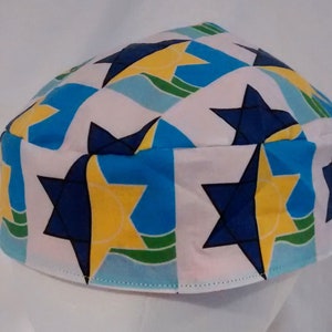 Op de afbeelding: Een witte kippa met een patroon van blauwe, gele en groene Davidsterren.