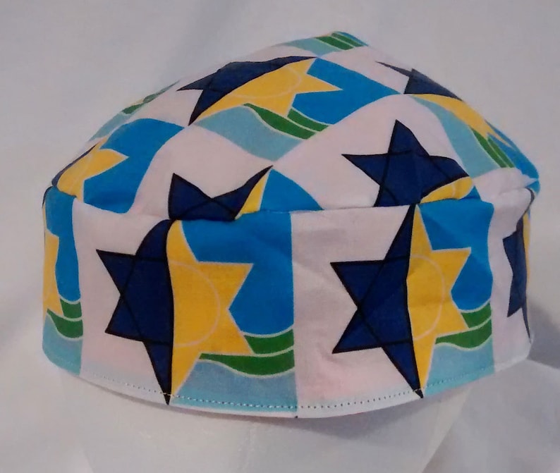 Op de afbeelding: Een witte kippa met een patroon van blauwe, gele en groene Davidsterren.