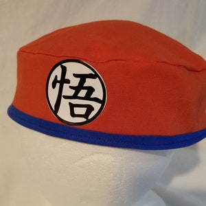 Op de afbeelding: Een rode en blauwe stoffen hoed met een witte cirkel en zwarte kanji-tekens. De kanji-tekens zijn "悟" en "空".