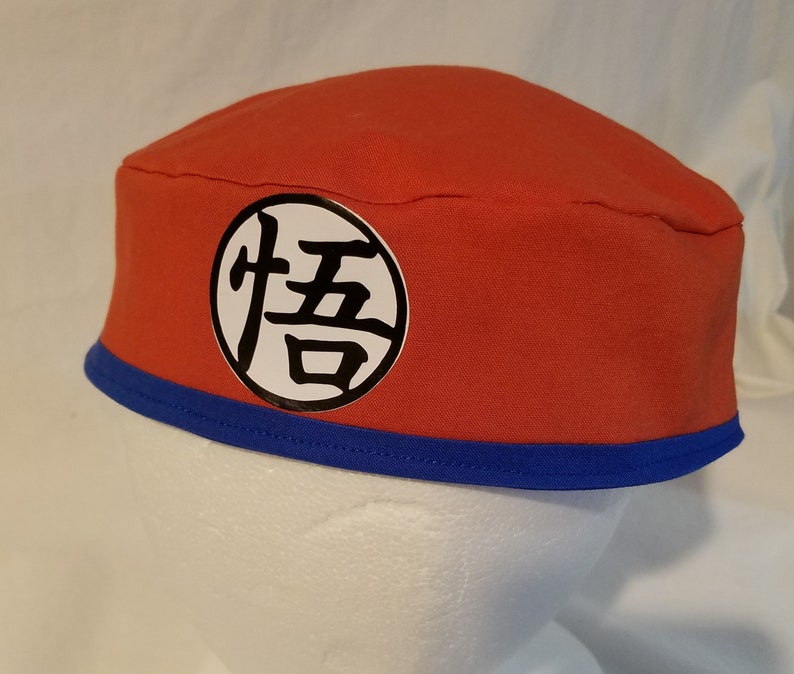 Op de afbeelding: Een rode en blauwe stoffen hoed met een witte cirkel en zwarte kanji-tekens. De kanji-tekens zijn "悟" en "空".