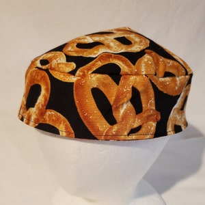 Op de afbeelding: Een zwarte stoffen kippa met een patroon van bruine pretzels. De kippa is een traditionele joodse hoofdbedekking.