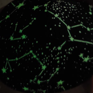 May include: Black fabric with a glow-in-the-dark constellation pattern. The fabric features green stars and lines connecting them, creating a celestial design.