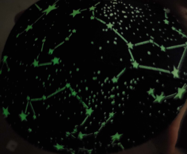 May include: Black fabric with a glow-in-the-dark constellation pattern. The fabric features green stars and lines connecting them, creating a celestial design.