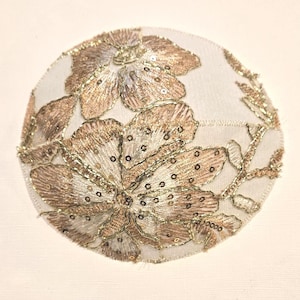 Op de afbeelding: Een witte stoffen kippa met gouden en bruine bloemenborduurwerk en pailletten.