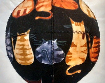 May include: A black fabric kippah with a colorful cat print. The cats are orange, brown, and gray. The kippah is round and has a stitched seam around the edge.