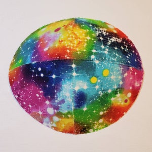 Pu&ograve; includere: Una kippah colorata con una stampa a galassia. La kippah &egrave; fatta di tessuto e ha uno sfondo bianco con un arcobaleno di colori e stelle bianche.