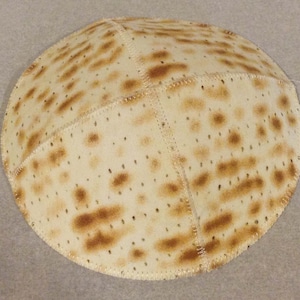 Può includere: Una matzah rotonda, beige, un tipo di pane azzimo, con un motivo marrone macchiato. La matzah è cucita in sezioni.