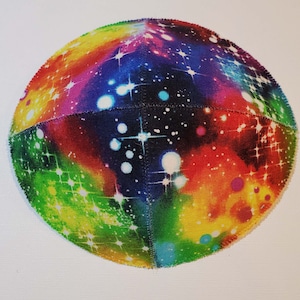 Pu&ograve; includere: Una kippah colorata con una stampa a galassia. La kippah &egrave; fatta di tessuto e ha una forma rotonda. Il tessuto &egrave; di colore blu scuro con un motivo arcobaleno di rosso, arancione, giallo, verde, blu e viola. Il tessuto &egrave; ricoperto di stelle bianche e punti bianchi.