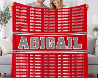 May include: A red fleece blanket featuring the repeated word BUCCANEERS in white and grey text, with the name ABIGAIL printed in large grey block letters across a central horizontal white stripe, bordered by thin grey lines.