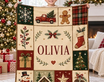 May include: A rectangular throw blanket featuring a grid of Christmas-themed illustrations including a red truck, gingerbread man, stocking, snowman, and a cabin. The center panel displays the name OLIVIA in large red letters.