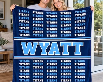 May include: A dark blue fleece blanket featuring a repeating pattern of the word TITANS in light blue and white text, with a large central horizontal band displaying the name WYATT in bold light blue letters outlined in white.