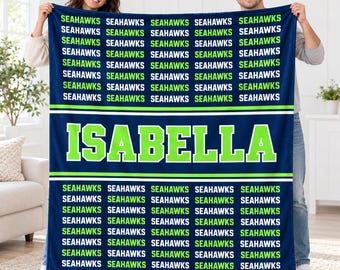 May include: A navy blue fleece blanket featuring a repeating pattern of the word SEAHAWKS in lime green and white text, with the name ISABELLA printed in large lime green block letters across the center section of the blanket.