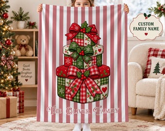 May include: A soft blanket featuring a vertical pink and white striped pattern with a central illustration of three stacked Christmas gift boxes adorned with red and green bows, holly leaves, and the text The Oliver Family printed below.