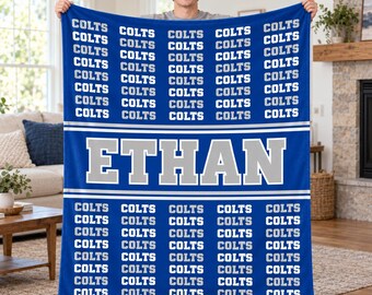 May include: A blue fleece blanket featuring a repeating pattern of the word COLTS in white and grey text. A large horizontal band across the center displays the name ETHAN in bold grey letters with a white outline, bordered by thin white stripes.