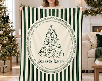 May include: A rectangular throw blanket featuring a dark green and cream vertical striped pattern. The center displays a cream circular emblem with a decorative border, containing a stylized Christmas tree made of bows and the text JOHNSON FAMILY.