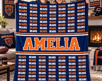 May include: A navy blue fleece blanket featuring a repeating pattern of the word BEARS in orange and white text. The center of the blanket displays the name AMELIA in large orange block letters, bordered by two horizontal white stripes.