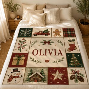 May include: A cream-colored throw blanket featuring a grid of Christmas-themed illustrations including a red truck, gingerbread man, snowman, gift, and pine trees. The center panel displays the name OLIVIA in large red letters.