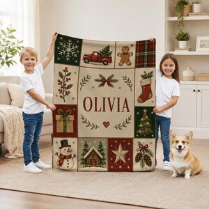 May include: A rectangular throw blanket featuring a grid of Christmas-themed illustrations including a red truck, gingerbread man, snowman, stocking, and pine trees. The center panel displays the name OLIVIA in large red letters.