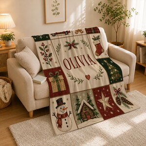 May include: A rectangular throw blanket featuring a grid of Christmas-themed illustrations including a snowman, a cabin, a gift, a stocking, and holly. The center panel displays the name OLIVIA in large red letters with a small red heart below.