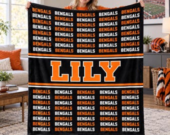 May include: A black rectangular fleece blanket featuring a repeating pattern of the word BENGALS in orange and white text. A central horizontal orange band displays the name LILY in large, bold, orange block letters with white outlines.