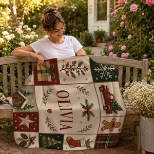 May include: A cream-colored throw blanket featuring a grid of Christmas-themed illustrations including a red truck, a gingerbread man, a stocking, a gift, and a star. The name OLIVIA is printed in large, dark red letters in the center.