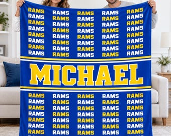 May include: A blue fleece blanket featuring a repeating pattern of the word RAMS in yellow and white text. A central horizontal band displays the name MICHAEL in large yellow block letters with a white outline against a blue background.