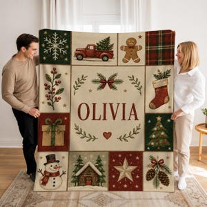 May include: A cream-colored throw blanket featuring the name OLIVIA in large red letters, surrounded by festive illustrations including a red truck, gingerbread man, snowman, Christmas tree, stocking, gift, and pinecones.