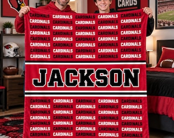 May include: A red fleece blanket featuring a repeating pattern of the word CARDINALS in black text, separated by horizontal black and white stripes, with the name JACKSON printed in large black block letters across the center.