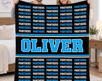May include: A black fleece blanket featuring a repeating pattern of the word PANTHERS in alternating white and light blue text, with a large light blue name OLIVER centered in a bold block font between two horizontal light blue stripes.